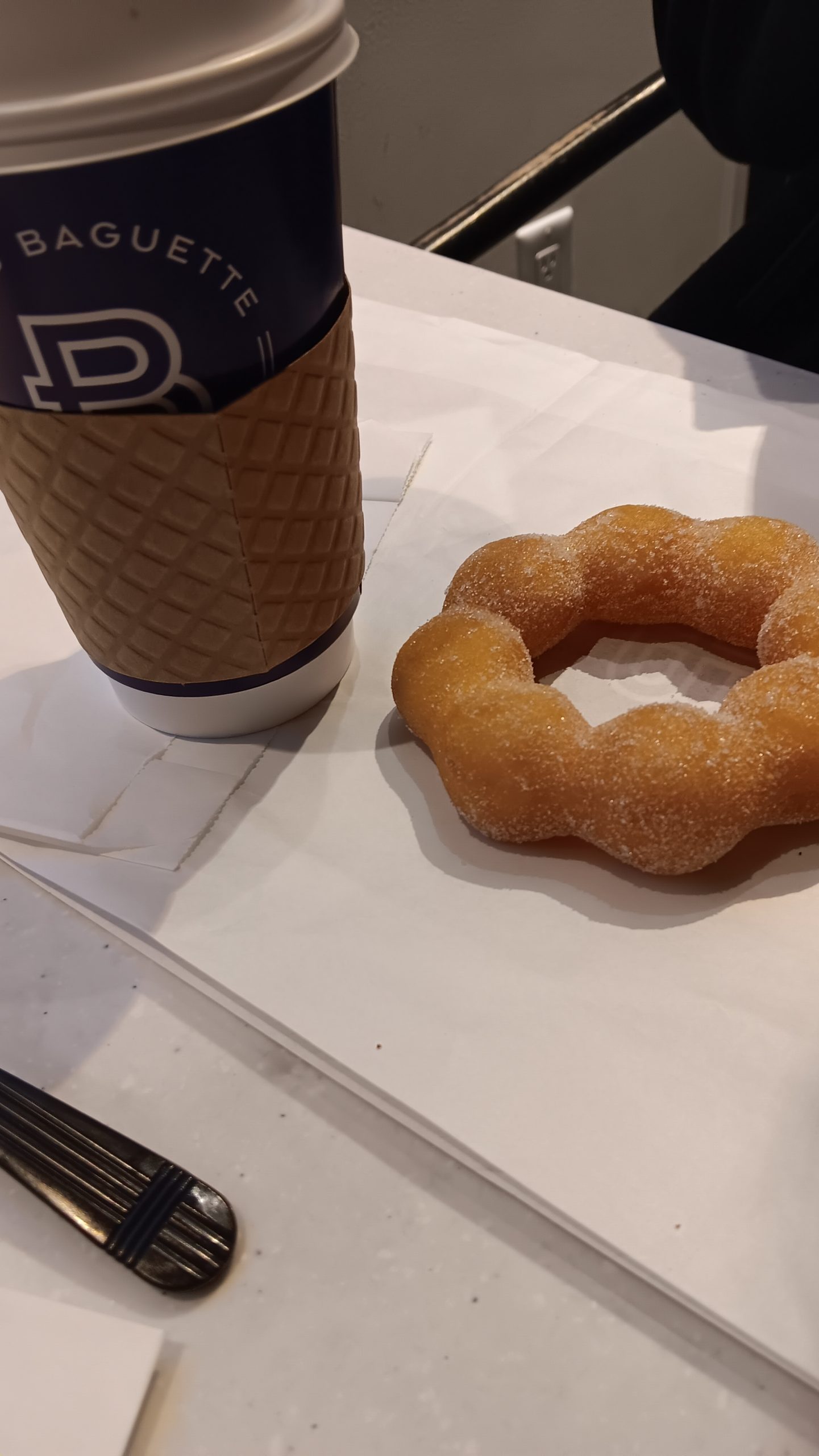 A coffee cup sits next to a sugared donut on a napkin