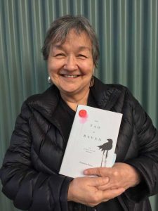 photograph of a Tlingit woman in a black jacket holding a book entitled Tao of Raven