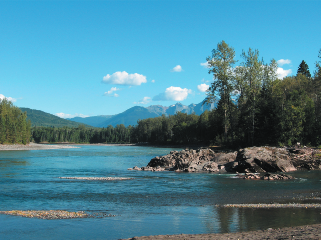 river landscape with rocks in the foregrounds, trees on the right in the middle ground, and mountains in the background