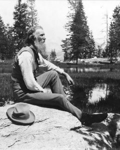 Black and white photo of a man sitting on a rock in front of a lake