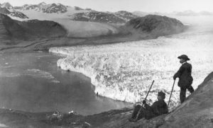 Two men appear on a hill looking out over a wide valley filled with glacial ice.