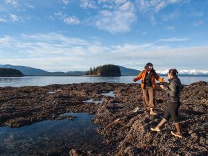 Two people conversing on the shore of an inlet.